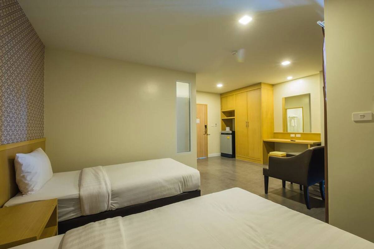 A hotel room with two beds, a desk, a chair, a kitchenette, and a bathroom.