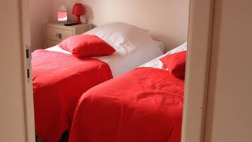 A bedroom with two beds, each with red bedding and white pillows. There is a bedside table with a lamp and a tissue box.