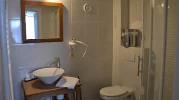 Un bany amb un tocador de fusta, un lavabo blanc, un mirall, un vàter i una zona de dutxa amb envàs de vidre.