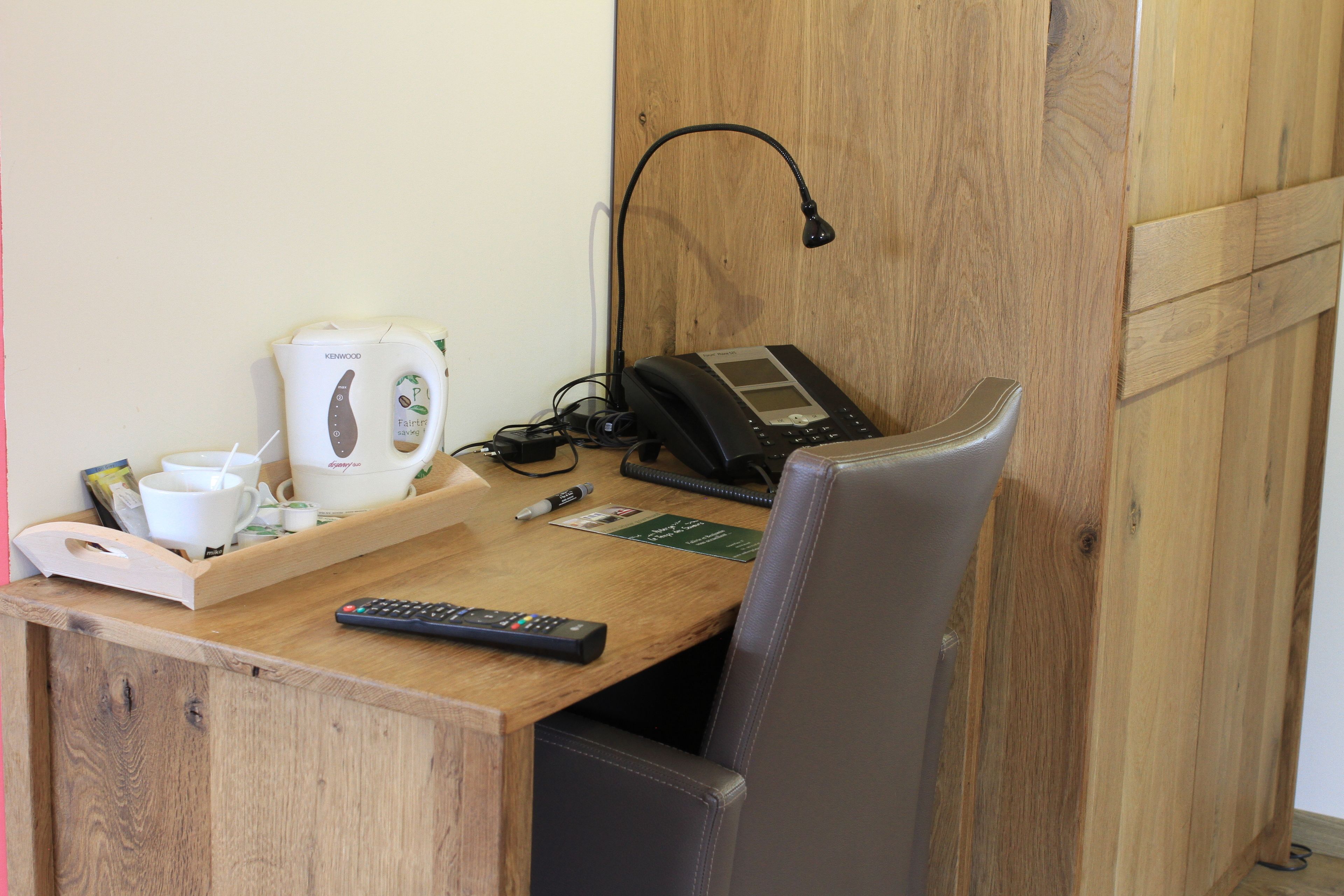 A wooden desk with a coffee maker, a phone, and a remote control.