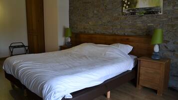 A bedroom with a wooden bed, a nightstand with a lamp, a wardrobe, and a stone wall.