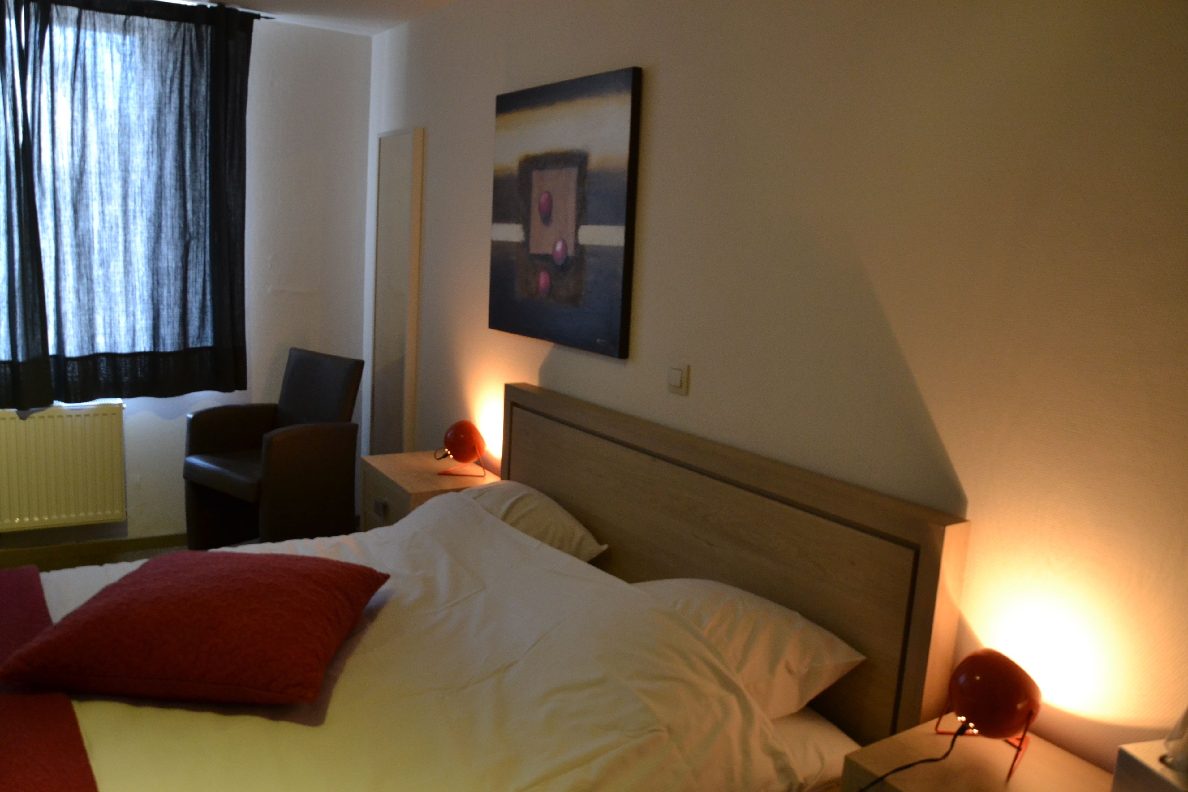 Una habitación de hotel con cama, una silla, una mesita de noche y una lámpara de pared.