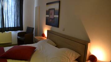 Una habitación de hotel con cama, una silla, una mesita de noche y una lámpara de pared.
