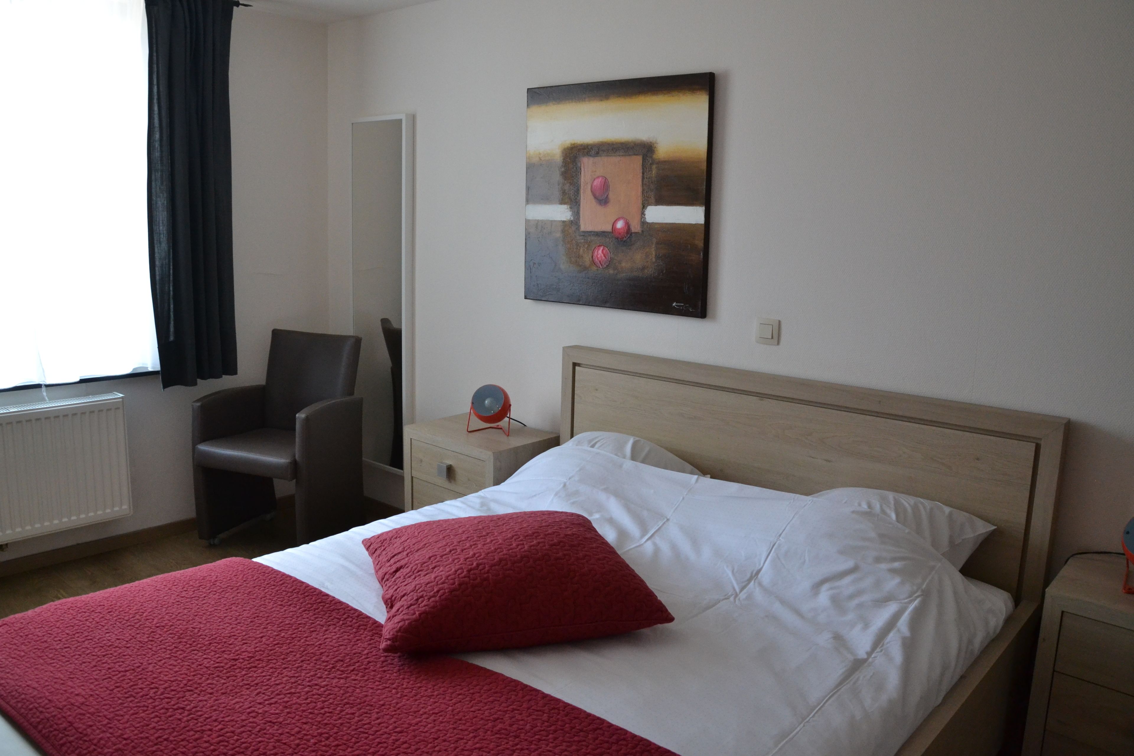 Een hotelkamer met een bed, een stoel, een nachtkastje, een wandklok en een schilderij.