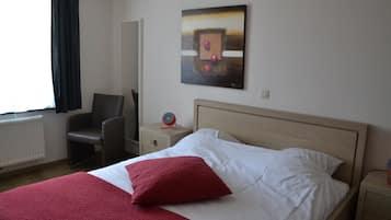A hotel room with a bed, a chair, a bedside table, a wall clock, and a painting.