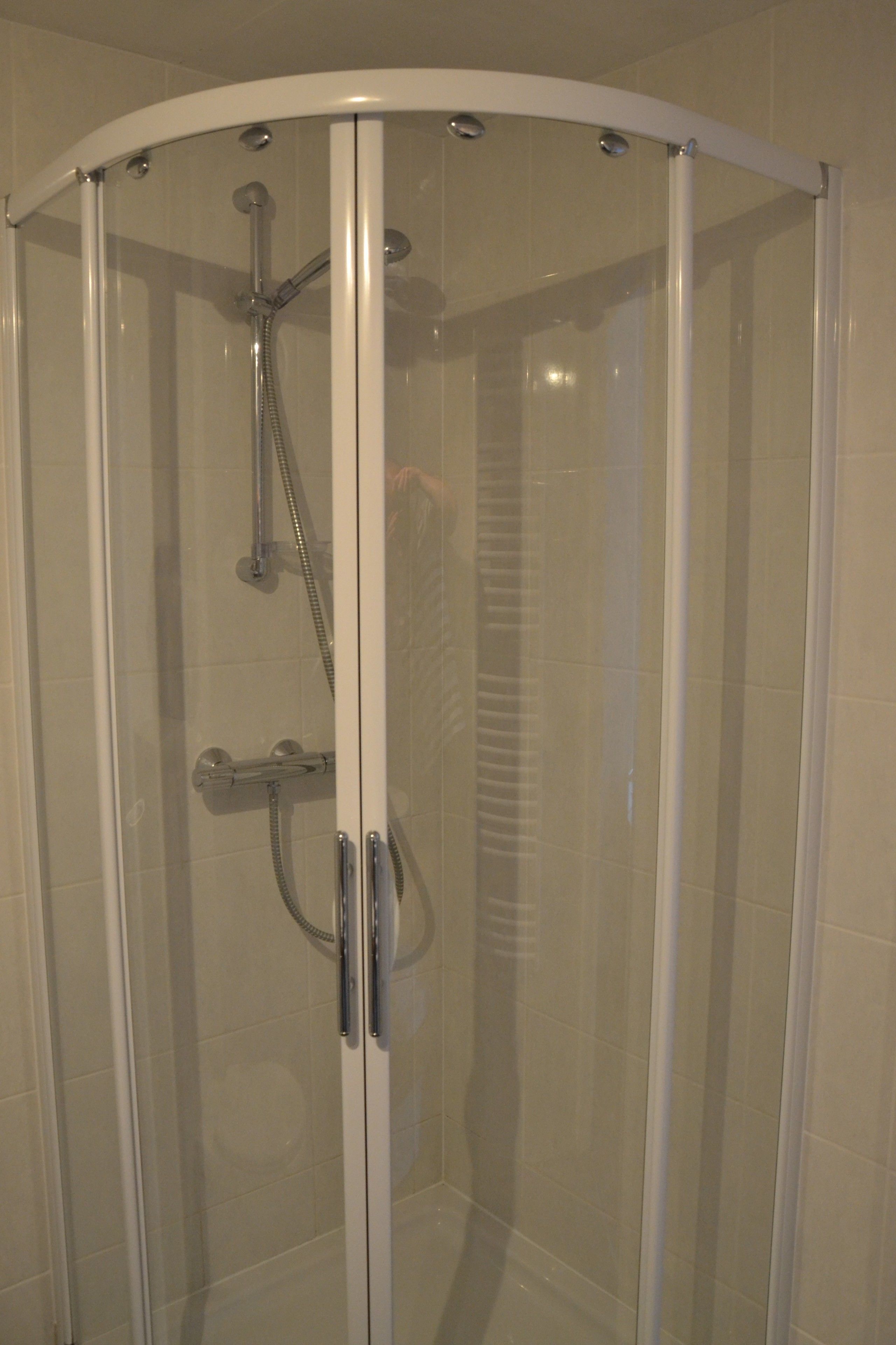 Une douche fermée par des parois en verre, dotée d’une porte incurvée et d’un pommeau de douche à main.