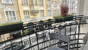 A balcony with a chair, a potted plant, and a view of a street with parked cars and buildings. - Residence Bílkova (Prague)