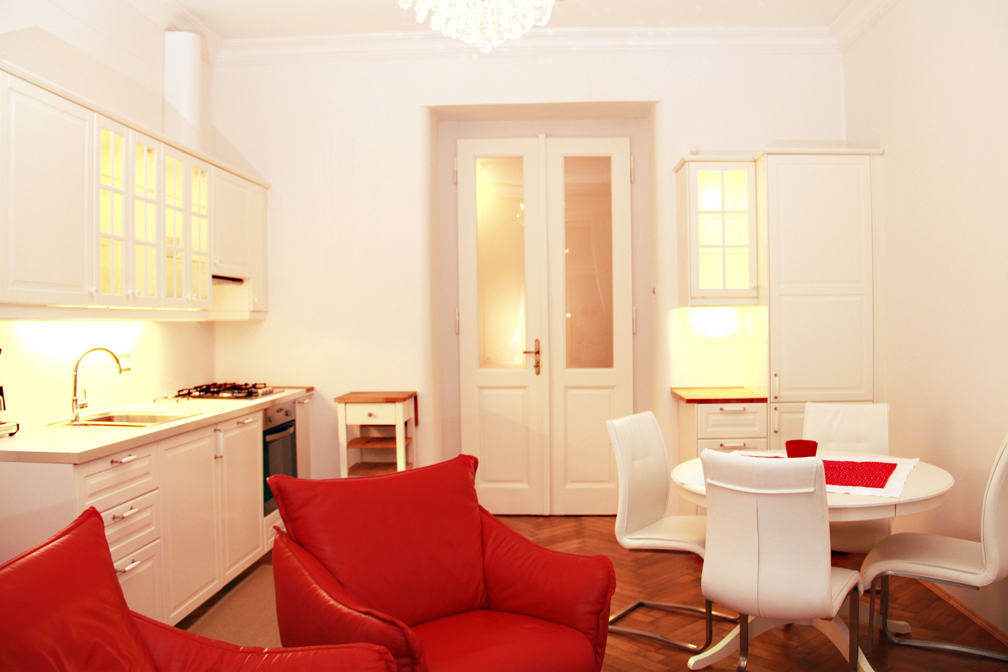 A modern kitchen with white cabinets, a dining area with a white table and chairs, and a red sofa.
