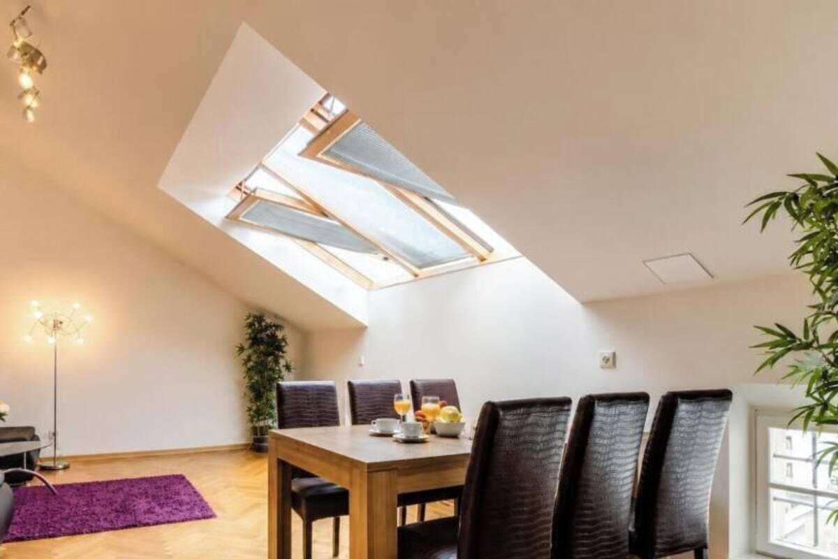 A modern loft apartment with a skylight, a dining area, and a living space with a sofa and a plant.