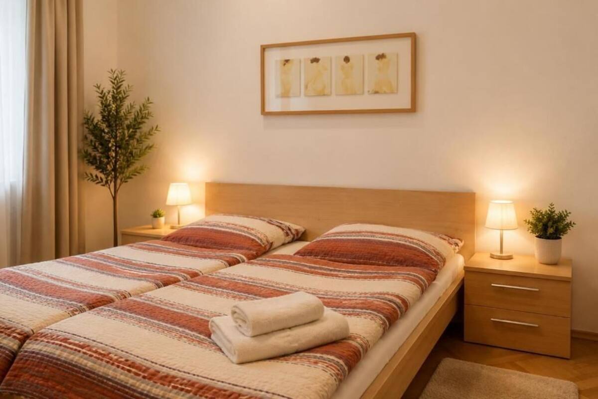 A double bed with striped bedding, bedside tables with lamps, a framed artwork above the bed, and a potted plant on one table.