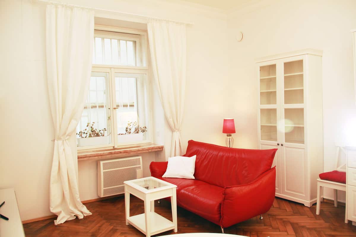 A room with a red sofa, white curtains, a white cabinet, and a small table.
