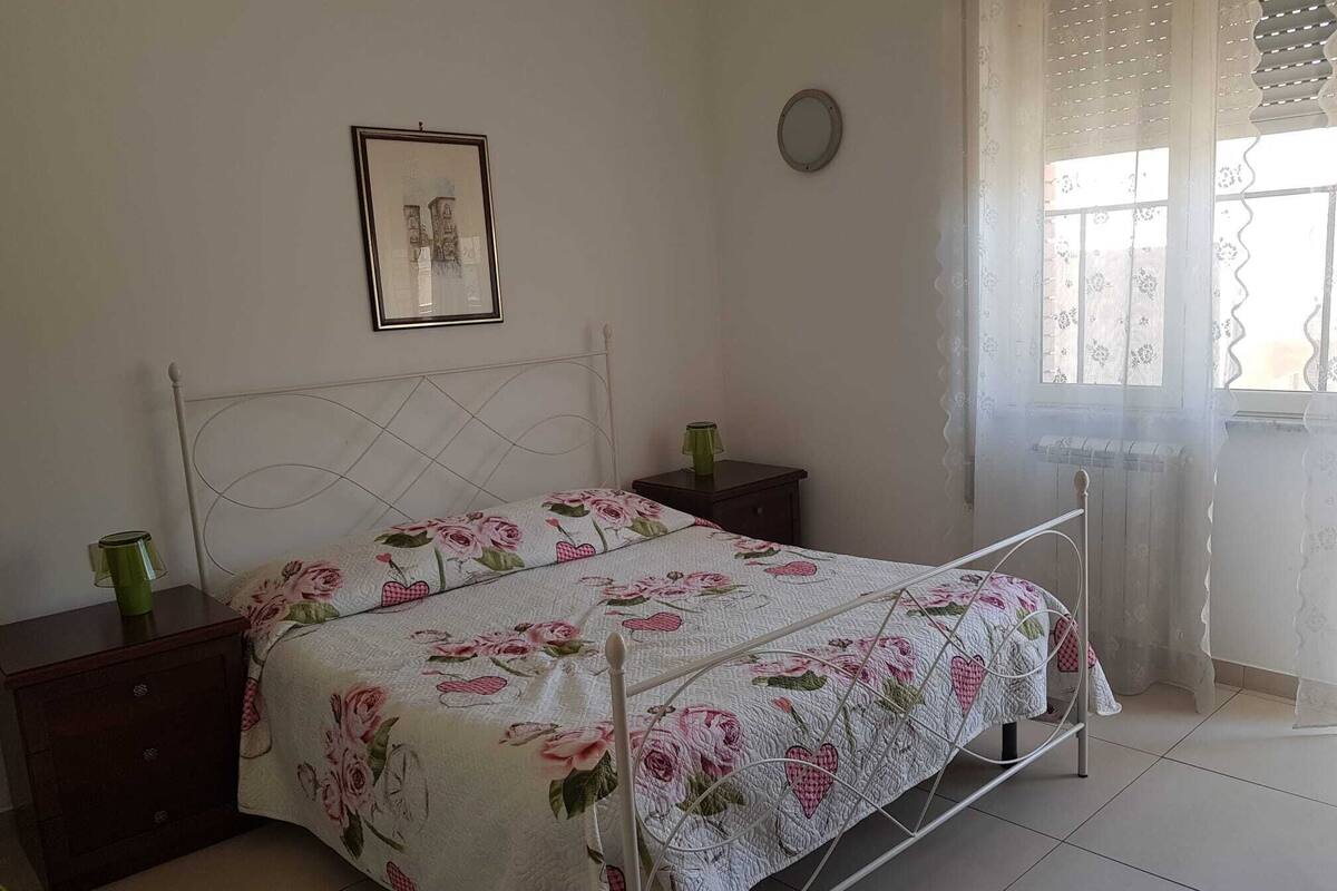 A bedroom with a bed, two bedside tables, a framed picture on the wall, and a window with curtains.