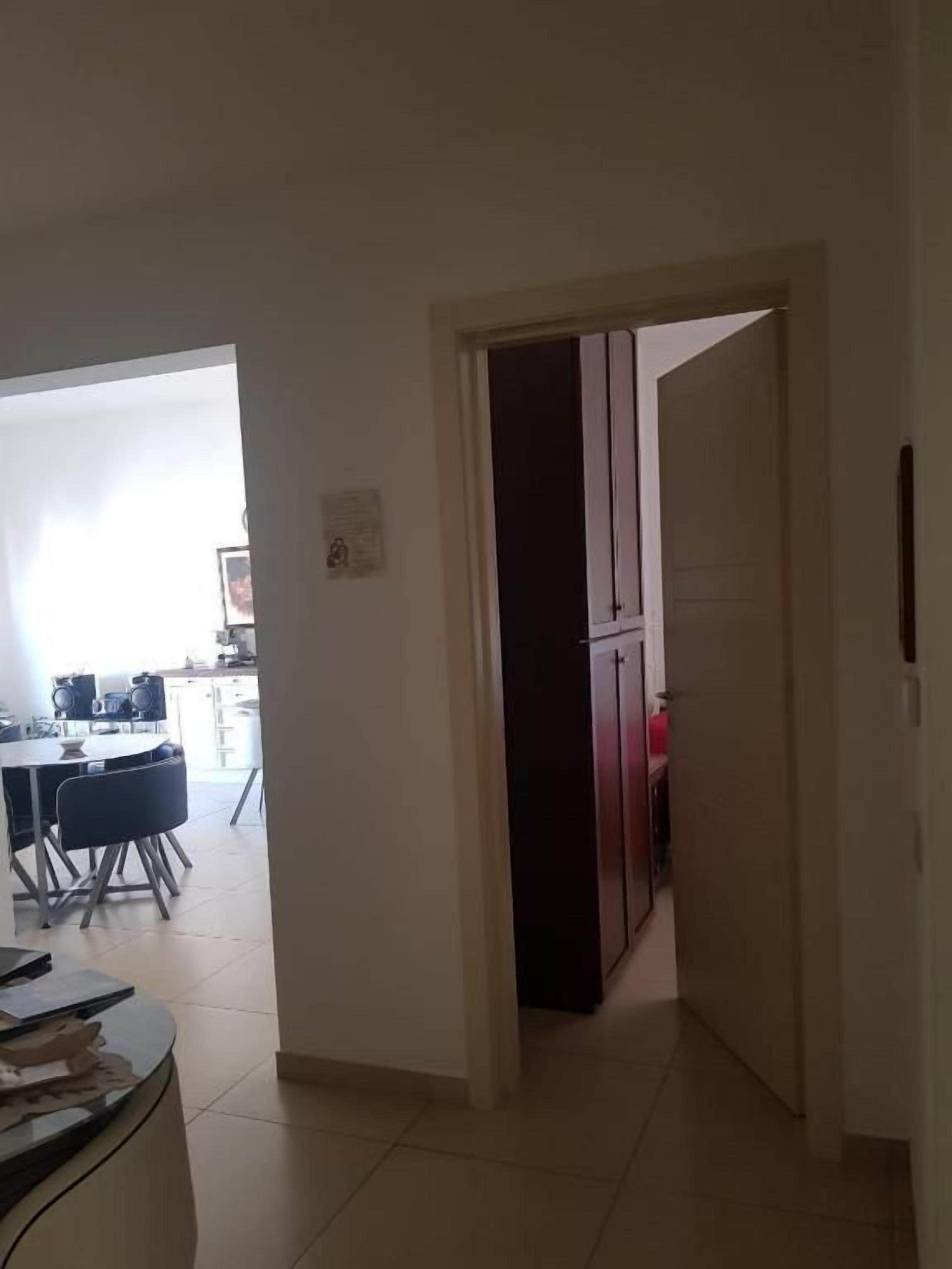 Un couloir mène à une cuisine équipée d’un réfrigérateur et d’une table à manger avec des chaises.