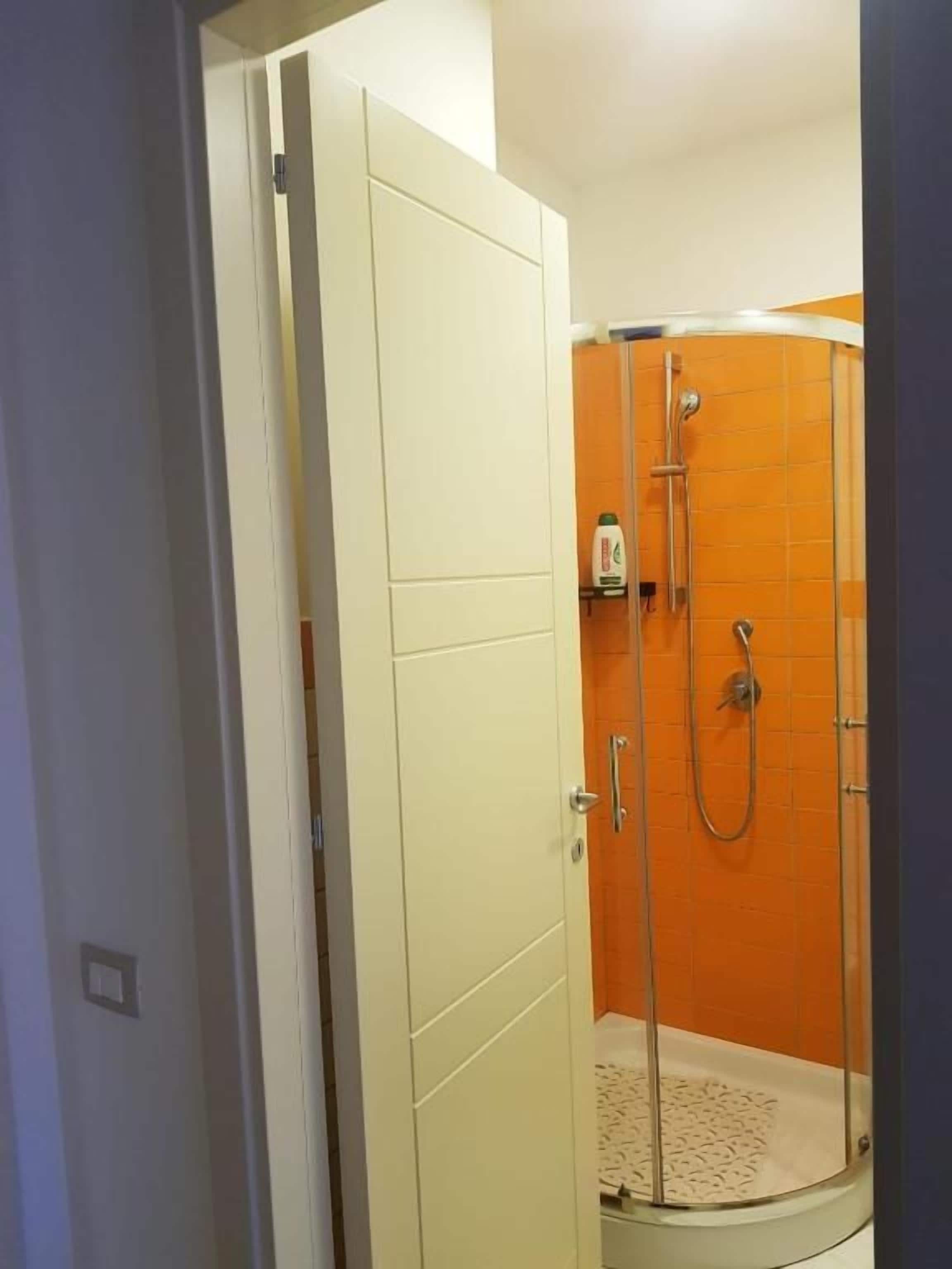 A shower with a glass door, a handheld showerhead, and a wall-mounted faucet.