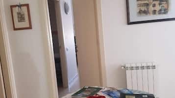 A room with a dining table covered with books and a red bowl, a framed picture on the wall, and a radiator.
