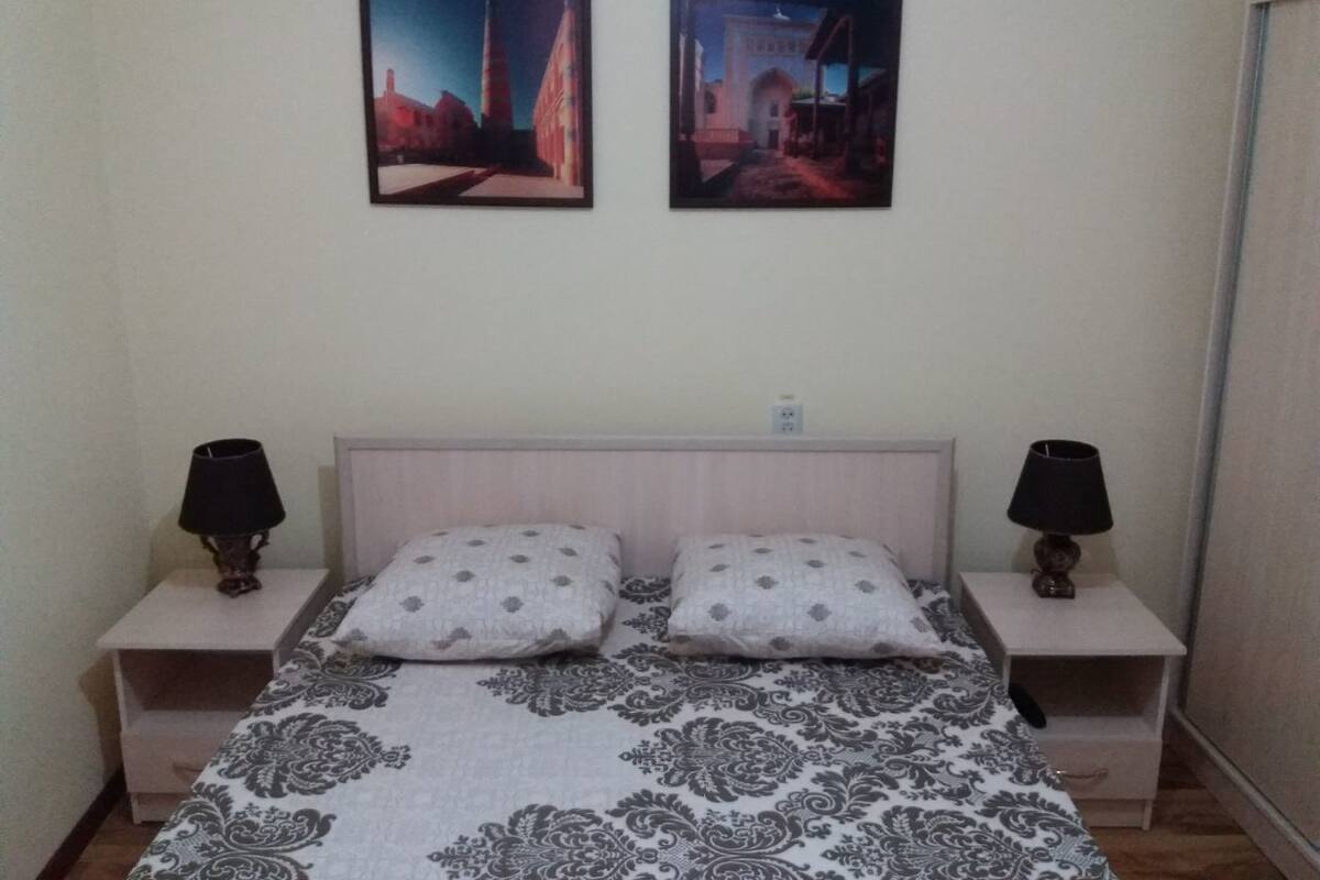 Quarto com cama, duas mesas de cabeceira, duas luminárias e duas molduras na parede.