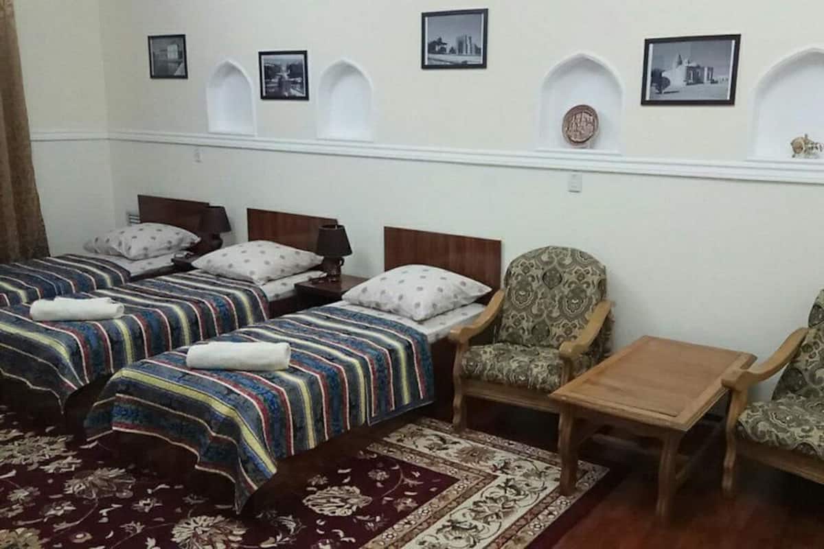 Quarto de hotel com duas camas, um sofá, uma mesinha e prateleiras decorativas na parede.