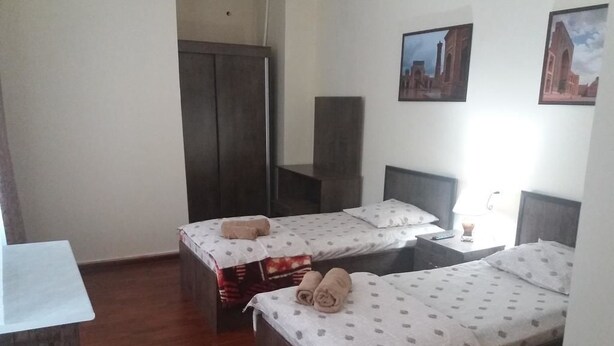 A room with two beds, wooden flooring, a desk, and a wardrobe. - Hotel Abu Shakheen (Bukhara)