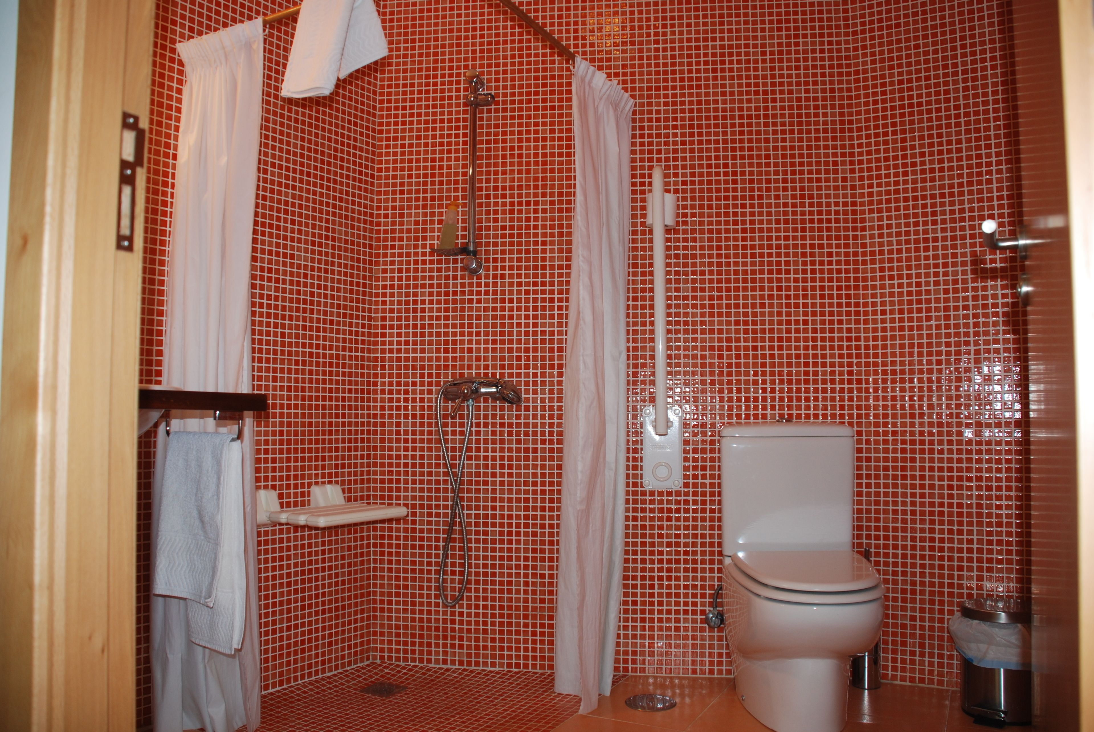 Un baño con paredes de azulejos rojos, ducha, inodoro y lavamanos.