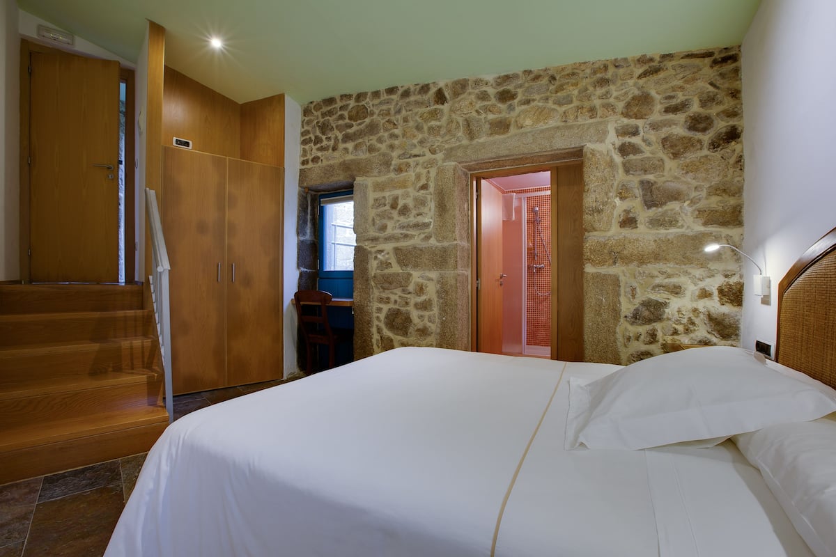 Un dormitorio con pared de piedra, armario de madera y cama con ropa de cama blanca.