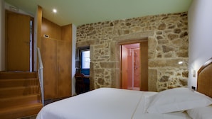 Un dormitorio con pared de piedra, armario de madera y cama con ropa de cama blanca.