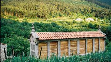 A rustic wooden building with a tiled roof, surrounded by lush greenery and hills in the background.