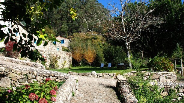 Un sendero de piedra conduce a un edificio rústico de piedra, con jardín y árboles.