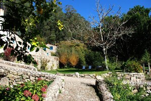 Un sendero de piedra conduce a un edificio rústico de piedra, con jardín y árboles.