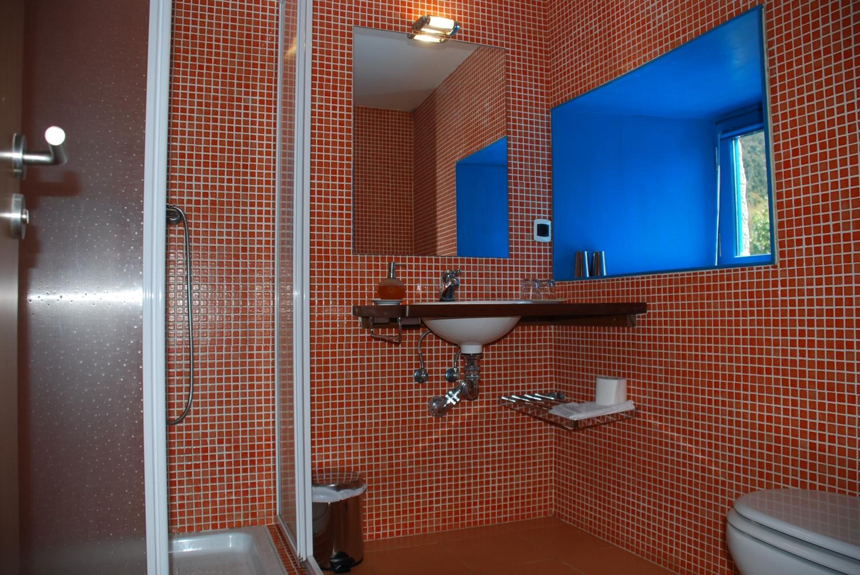 A bathroom with red tiled walls, a white sink, a mirror, and a window.