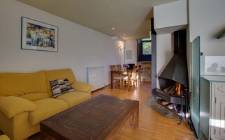 Una sala de estar con un sofá amarillo, una mesa de centro de madera, una chimenea y un comedor con sillas y una mesa.