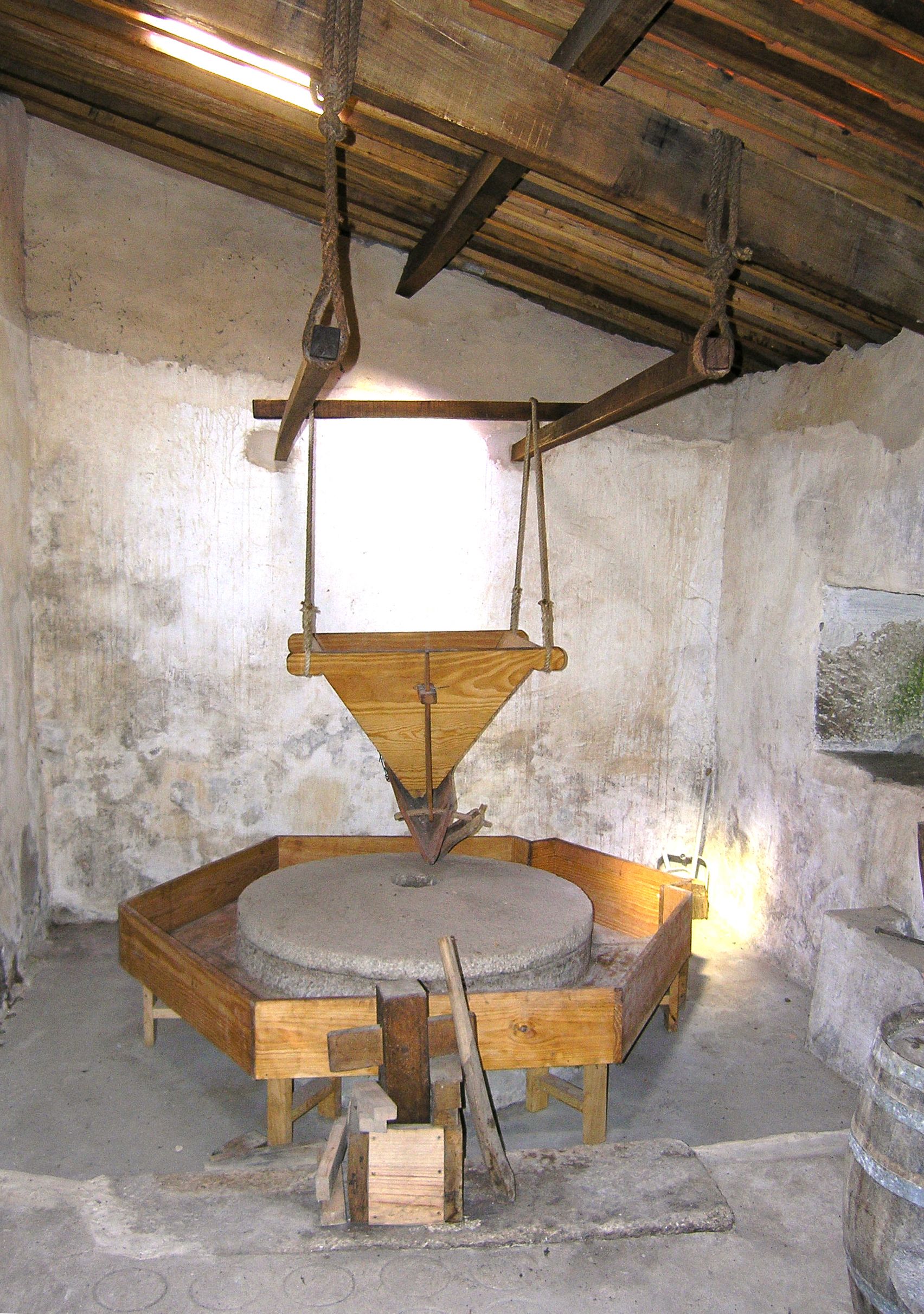 A rustic room with a wooden table, a hanging pulley system, and a stone wall.