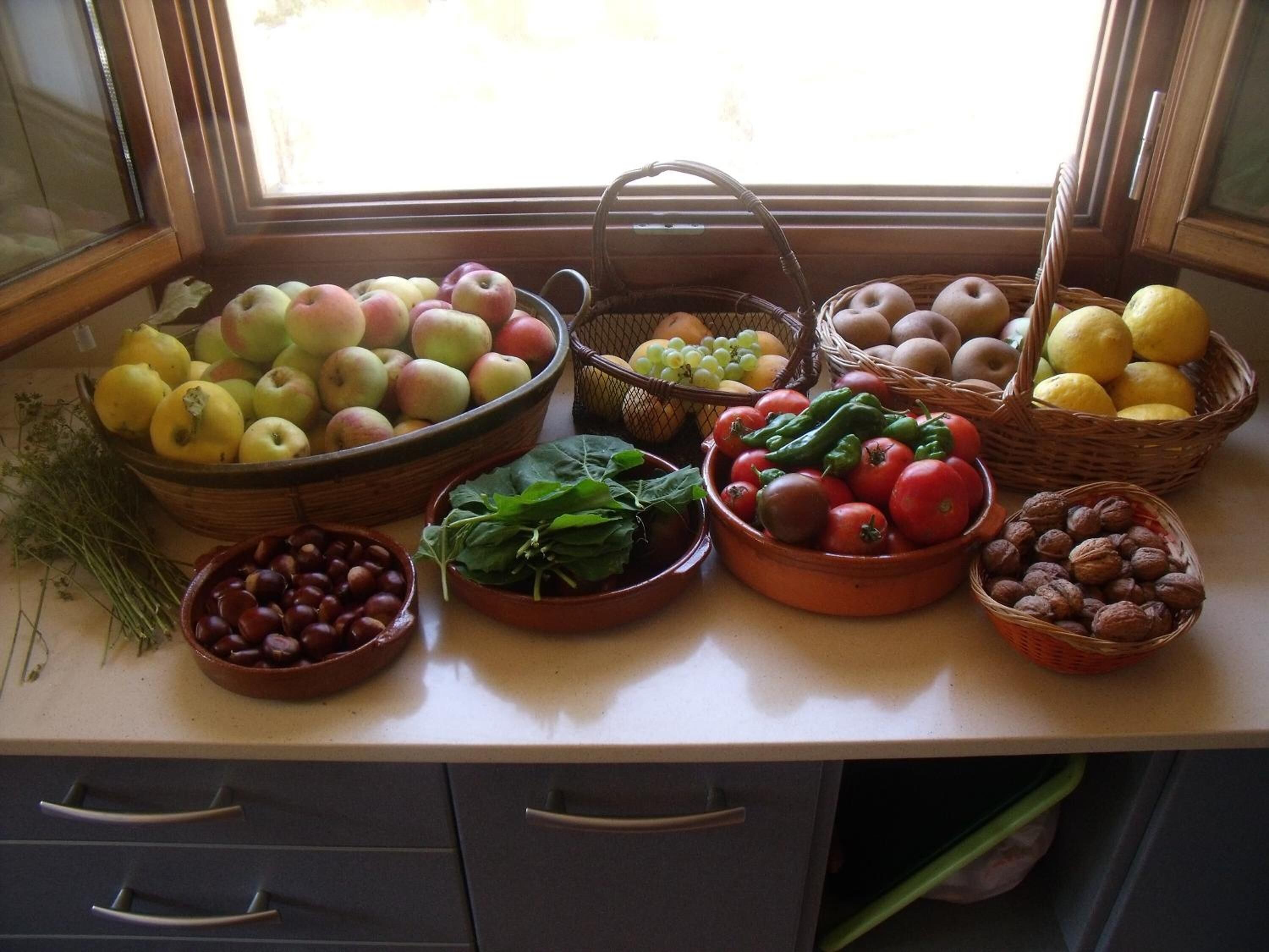 A kitchen counter with various fruits and vegetables, including apples, grapes, tomatoes, and leafy greens.