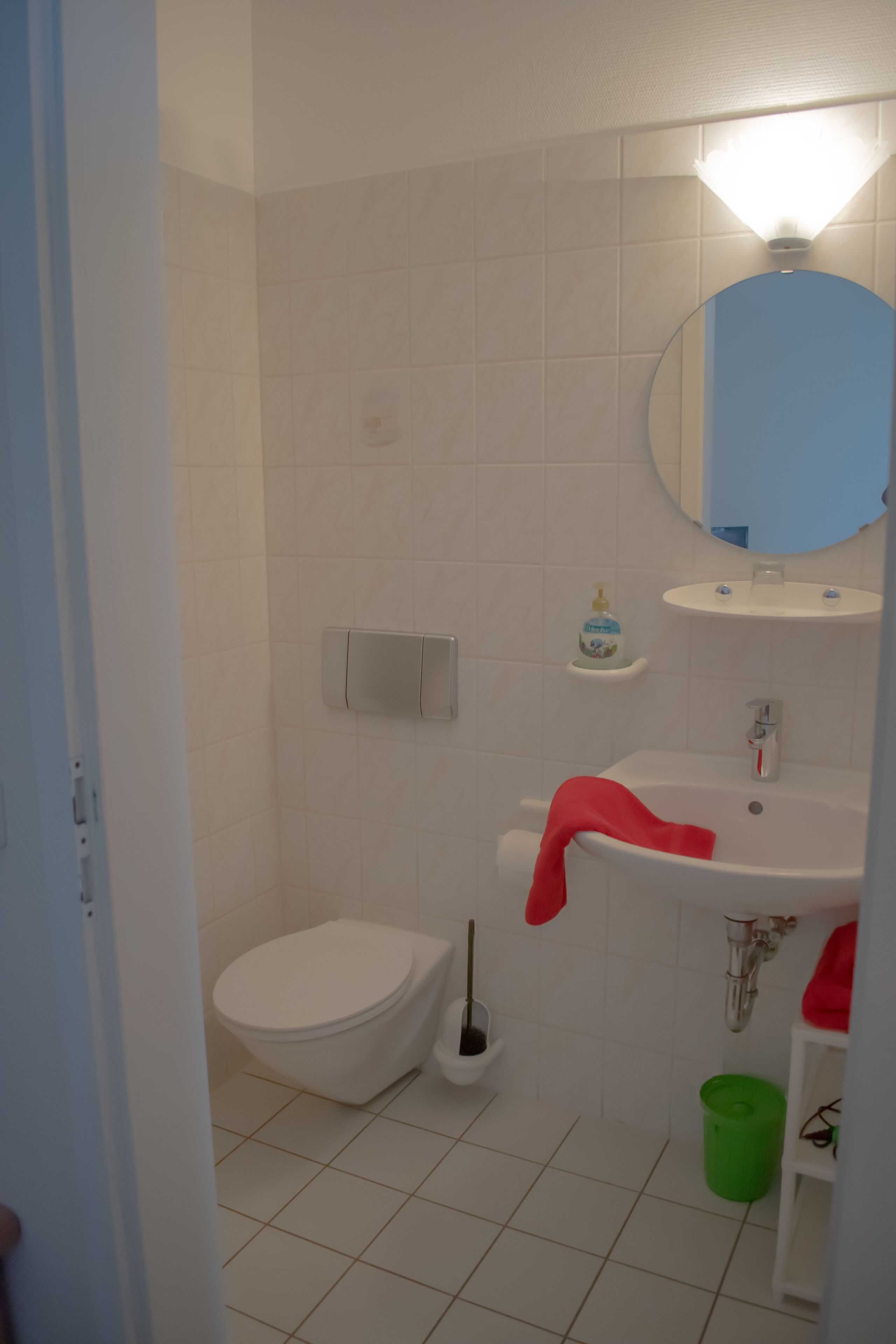 Un baño con inodoro, lavamanos, espejo y un cubo de basura verde.