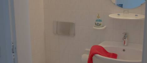 Un baño con inodoro, lavamanos, espejo y un cubo de basura verde.