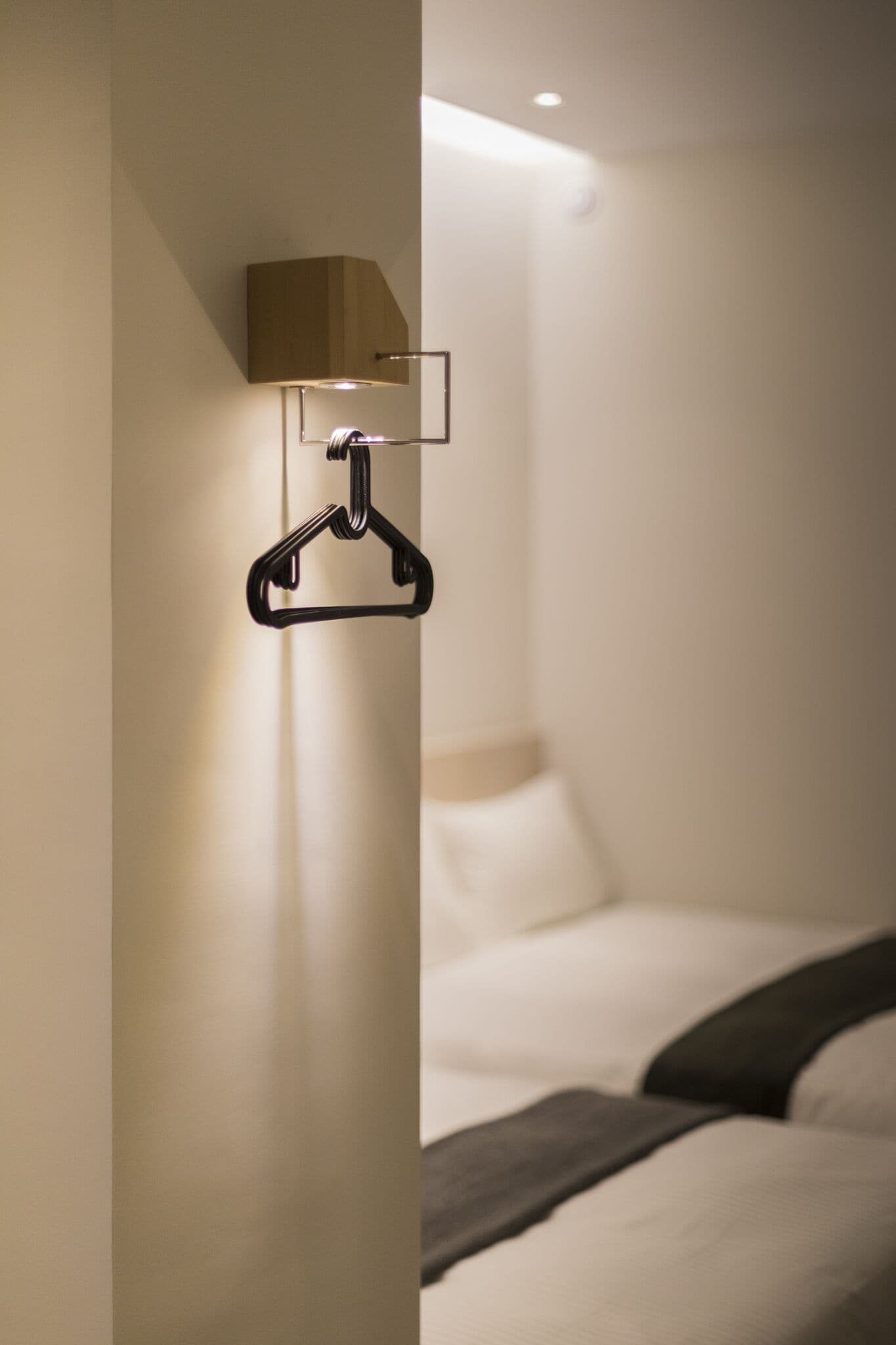 A hotel room with a bed, a wall-mounted light fixture, and a hanging coat hook.