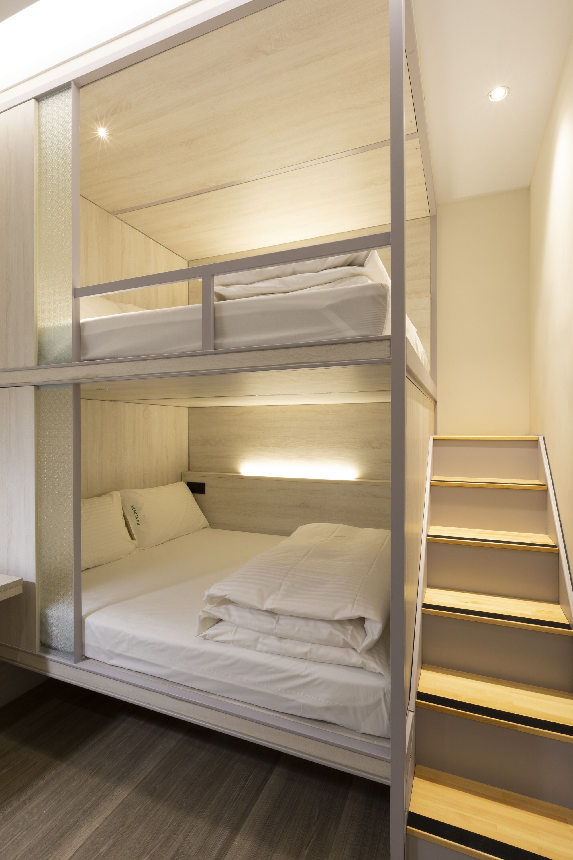 A bunk bed room with a wooden floor, a staircase, and a wall-mounted shelf.