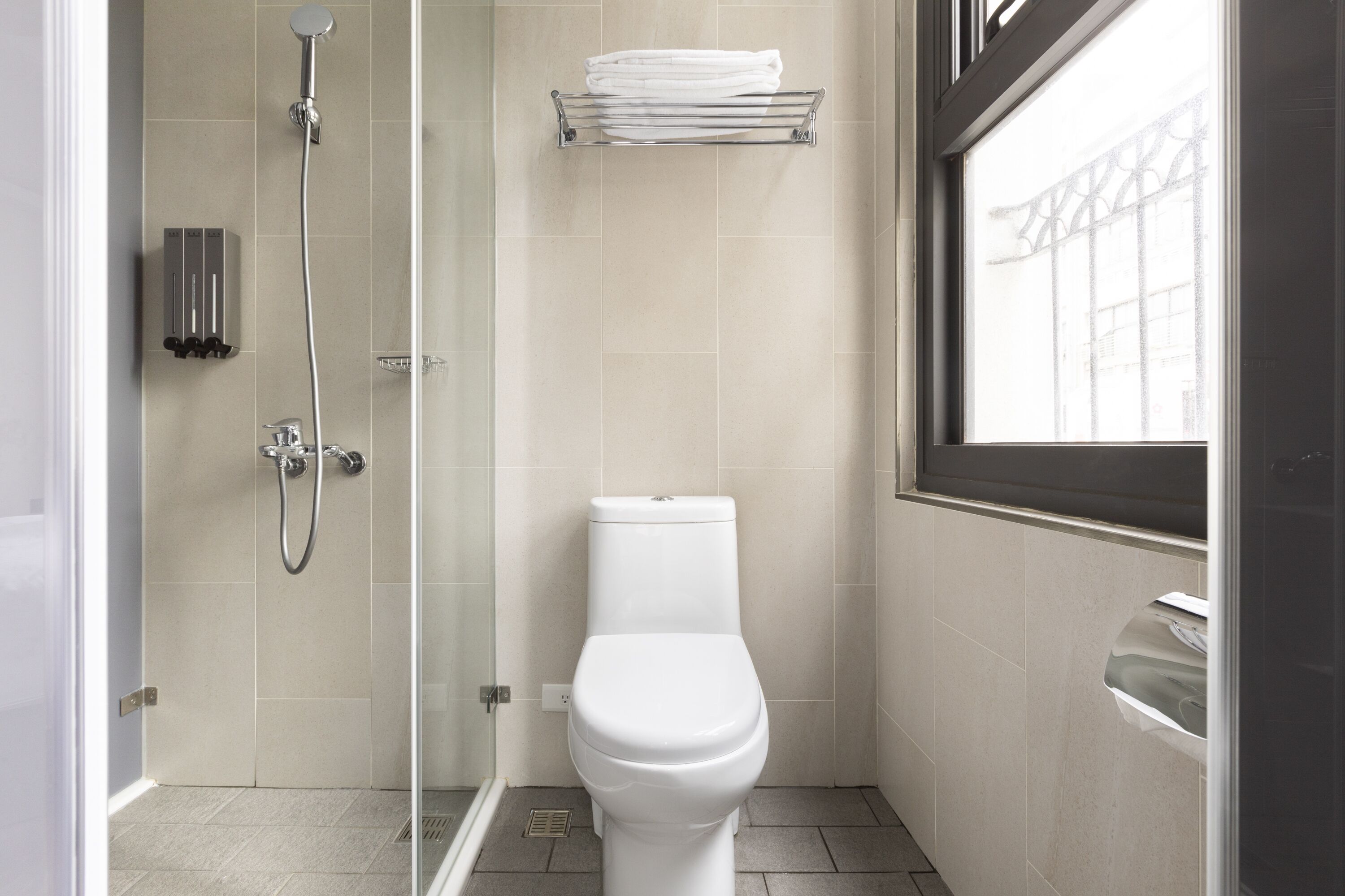 A modern bathroom with a glass-enclosed shower, a white toilet, and a towel rack above it.