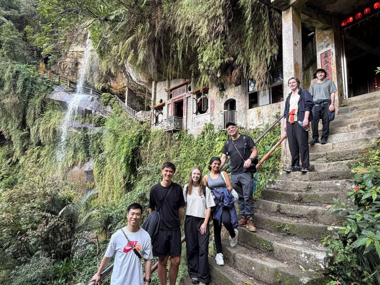 Eine Gruppe von Personen steigt eine Steintreppe hinauf, im Hintergrund ein Wasserfall.