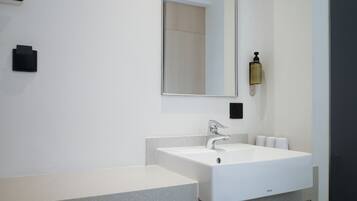 A modern bathroom with a white sink, a large mirror, and a towel dispenser.