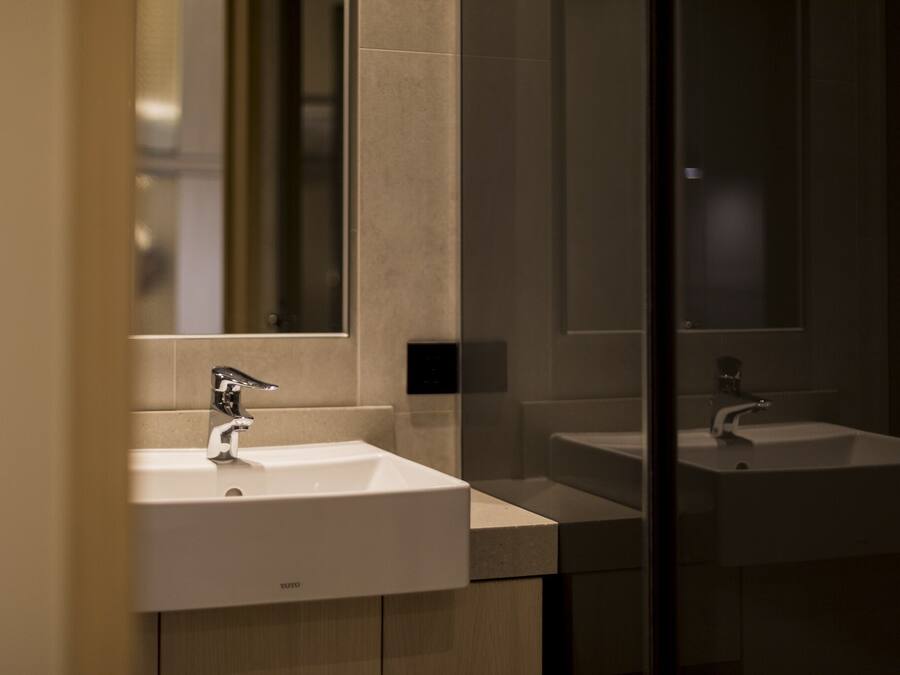 A modern bathroom with two sinks, a mirror, and a light switch on the wall.