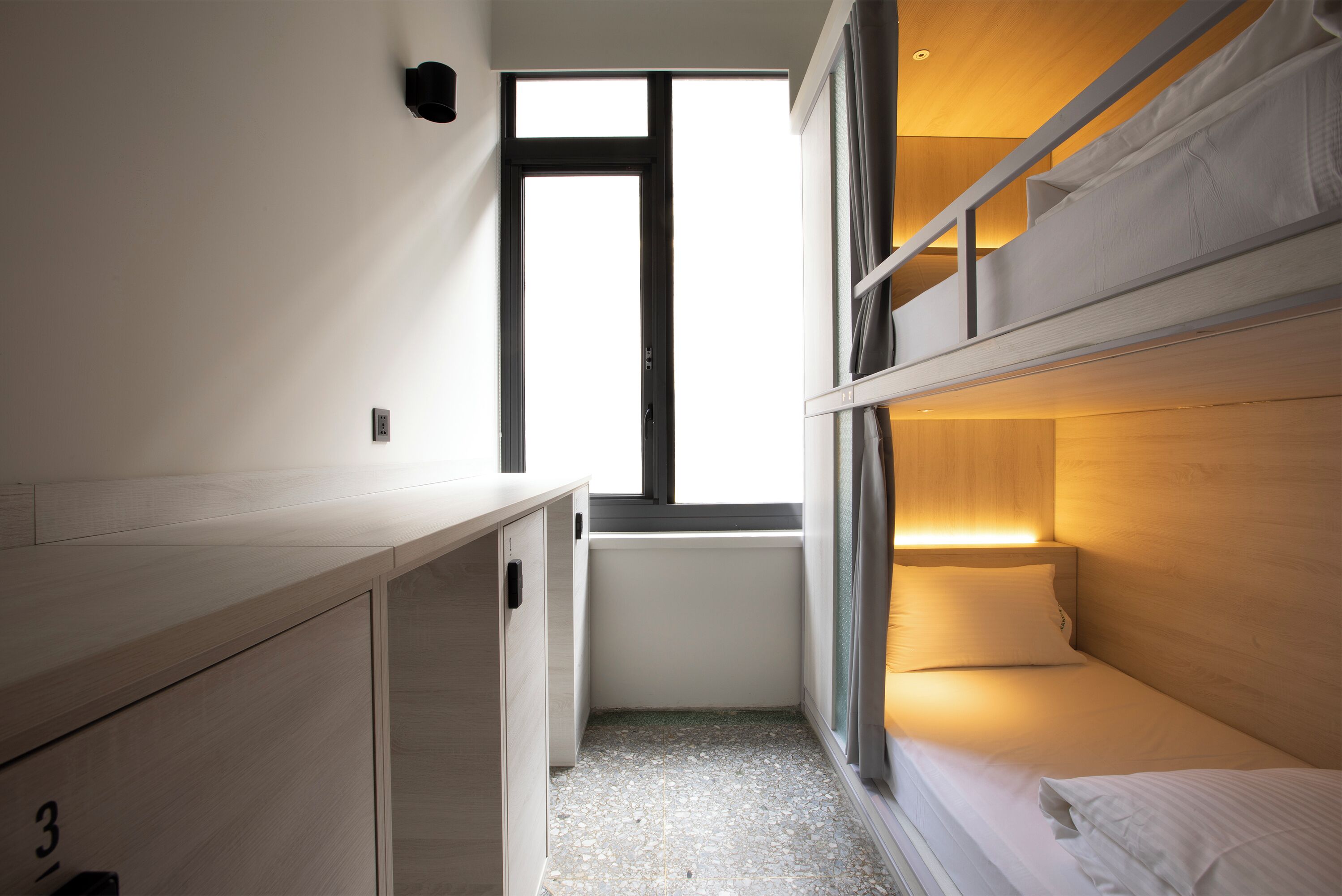 A compact room with bunk beds, a small desk, and a window providing natural light.