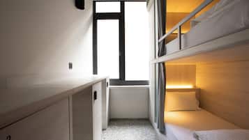 A compact room with bunk beds, a small desk, and a window providing natural light.