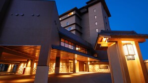 Een moderne hotelentree met een overdekte doorgang, stenen zuilen en een goed verlichte gevel.