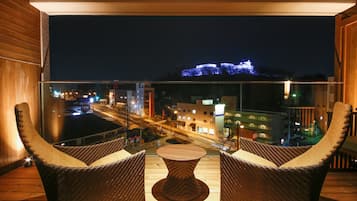 Un balcón con sillas de mimbre y una mesa, con vistas a un paisaje urbano nocturno.