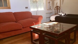 Una sala de estar con un sofá rojo, una mesa de centro de cristal, una lámpara y obras de arte en las paredes.