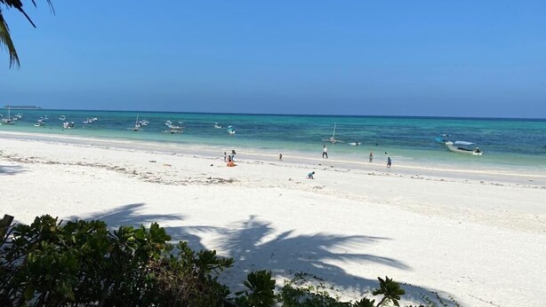 Une plage de sable blanc, une eau turquoise et limpide, et plusieurs bateaux ancrés au loin.