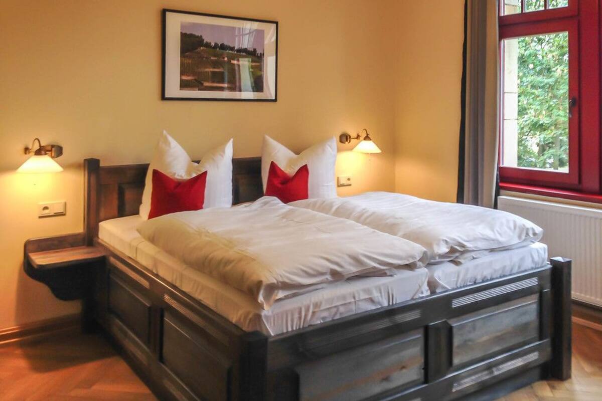 A double bed with white bedding, two nightstands with lamps, a framed picture on the wall, and a window with a red frame.
