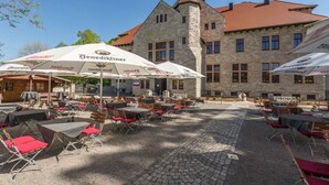 An outdoor café with tables and chairs, surrounded by stone buildings with red roofs. - Waldschlösschen Wangen (Nebra)