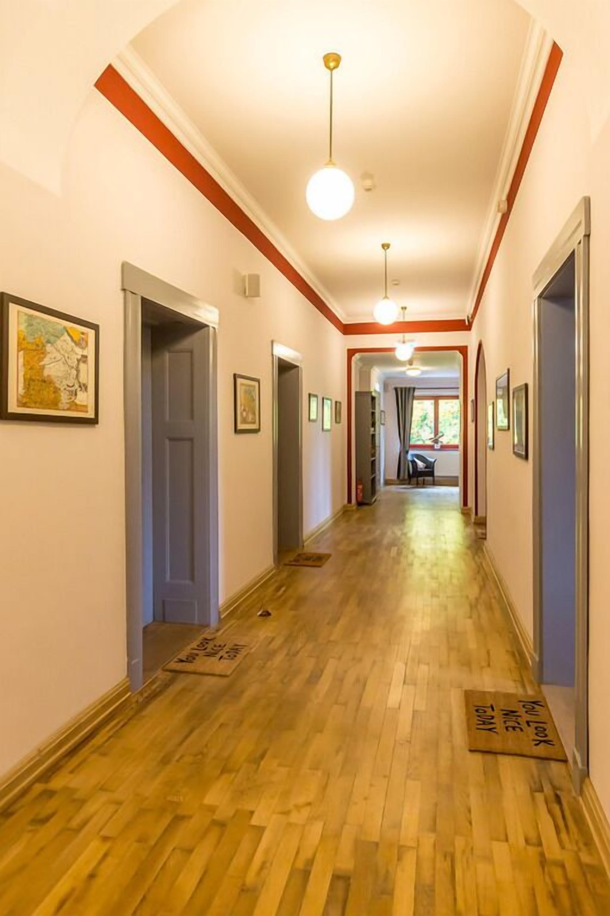 Un pasillo con piso de madera, obras de arte enmarcadas en las paredes y una puerta al final que da a una habitación.