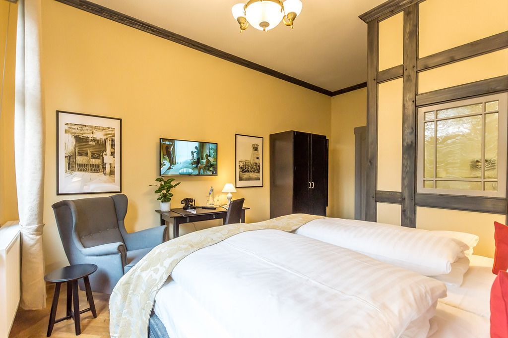 Una habitación de hotel con una cama grande, un escritorio con silla, televisión y cuadros en la pared.